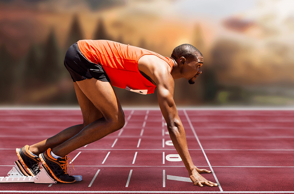 Man in orange tank top and black shorts at starting line of track