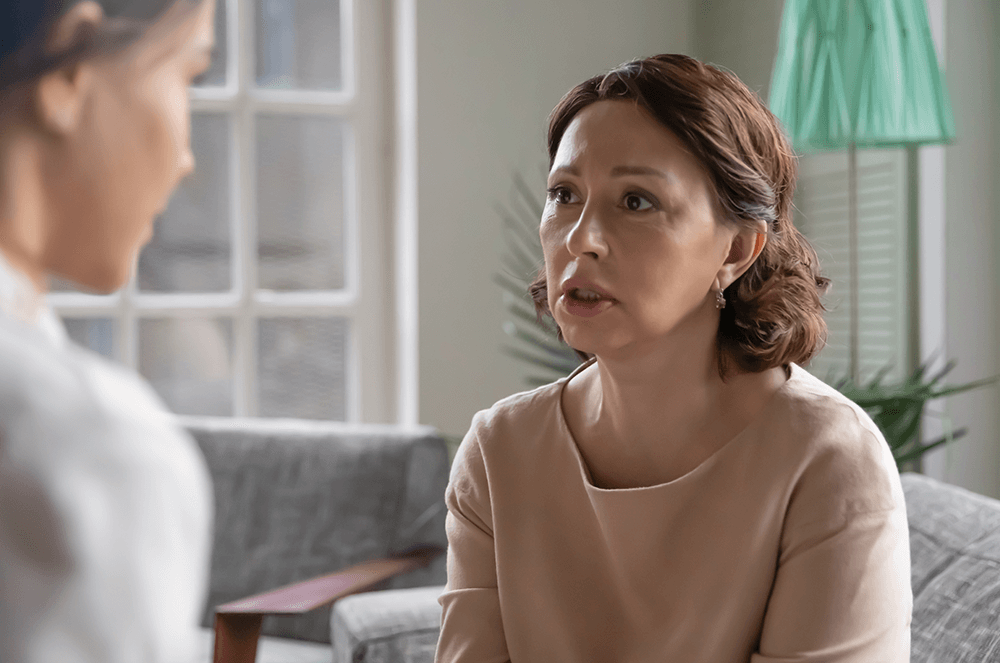 Woman apologizing to another woman while sitting on couch