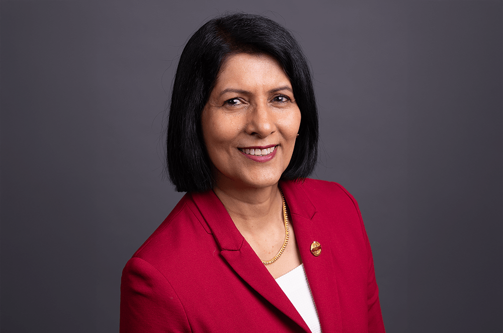Toastmasters International President Radhi Spear in red suit jacket with Toastmasters pin