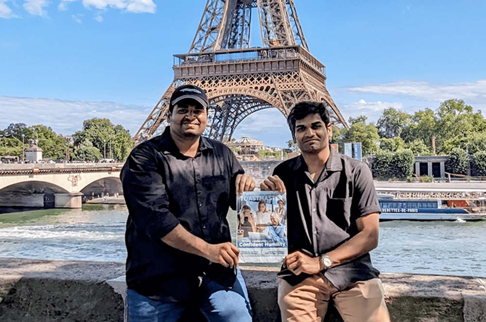 Two men posing with the Toastmaster magazine in front of the Eiffel Tower