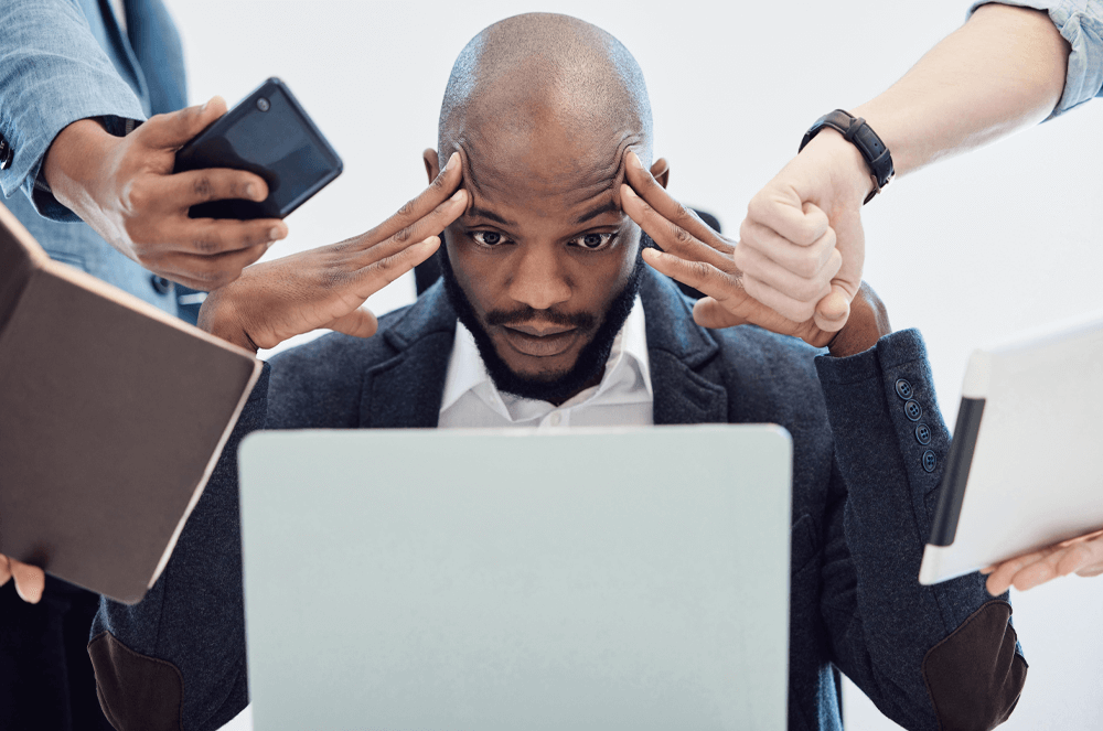 Man at laptop with people handing him phones, notebooks, and other items