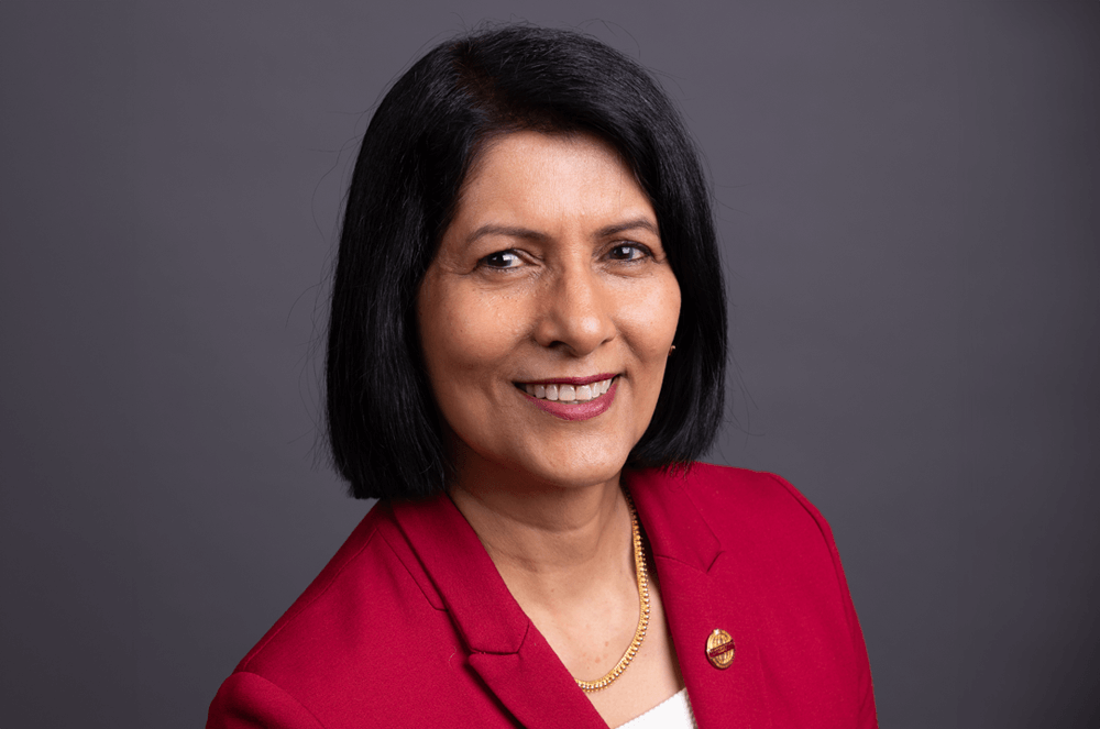 Toastmasters International President Radhi Spear in red suit jacket with Toastmasters pin