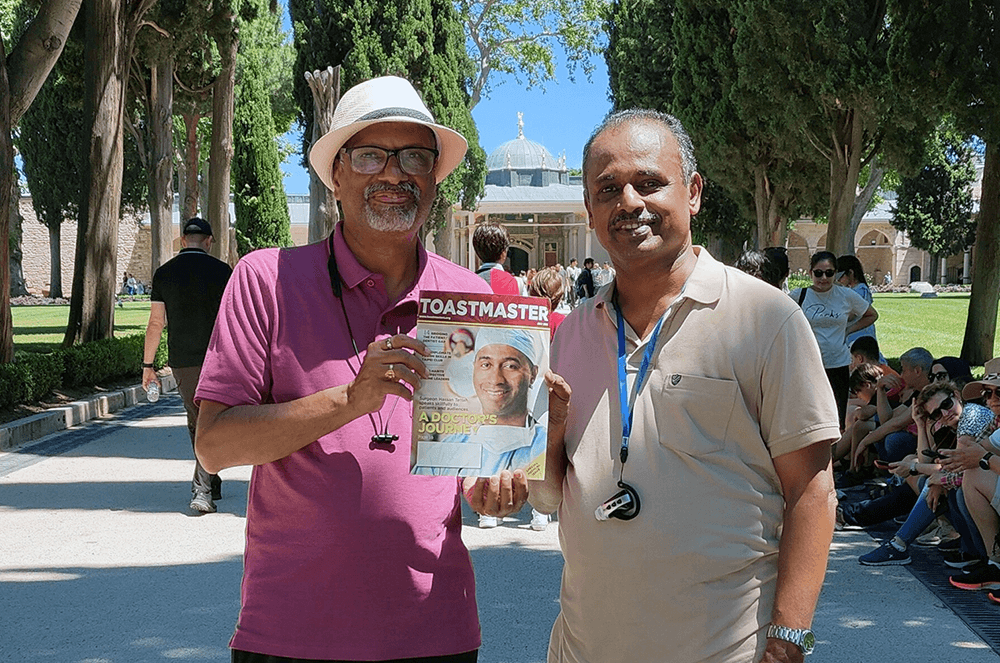 Two men posing with the Toastmaster magazine in front of building in Turkey