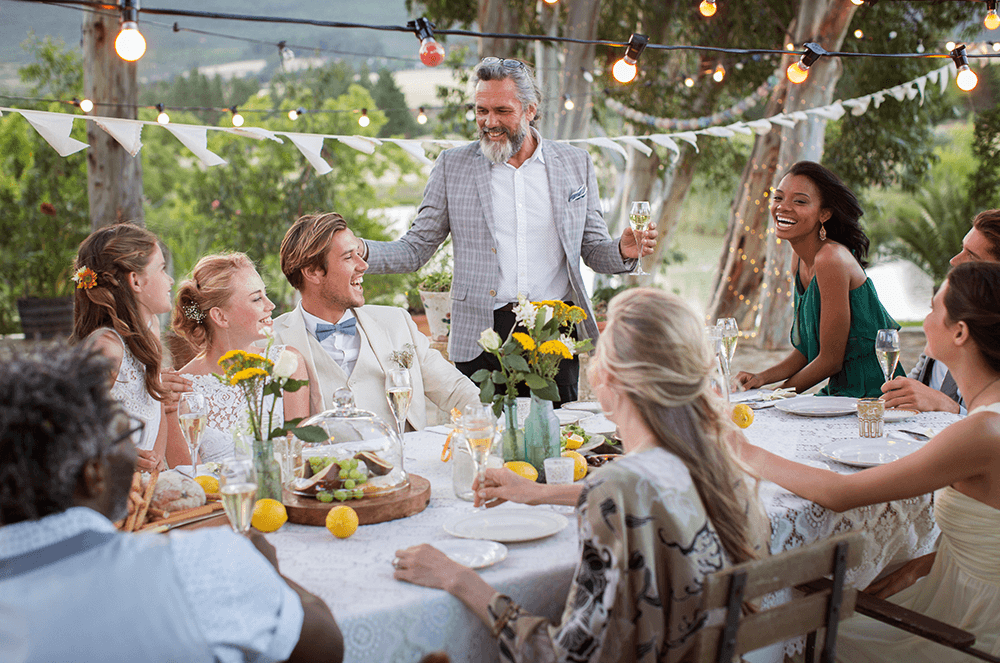 Man standing and toasting with people sitting at table laughing