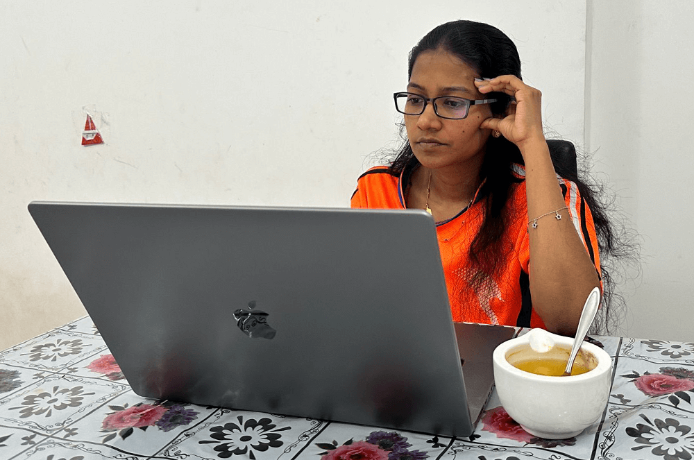 Woman working on a laptop sitting next to a bowl of chicken soup