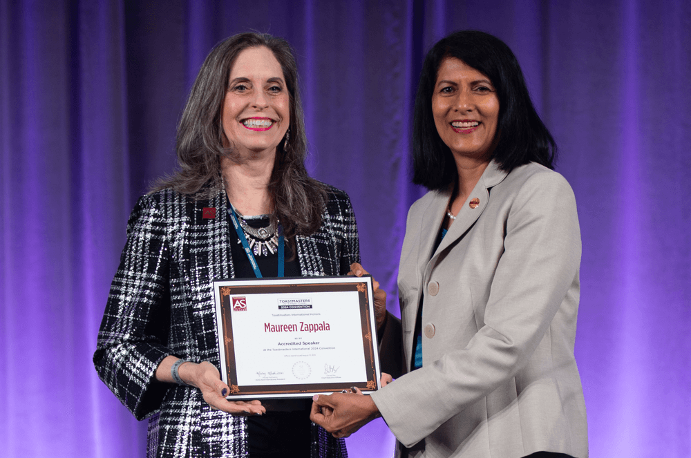 Two women posing onstage with award against purple background