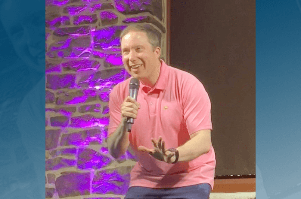 Man in pink shirt speaking into microphone onstage