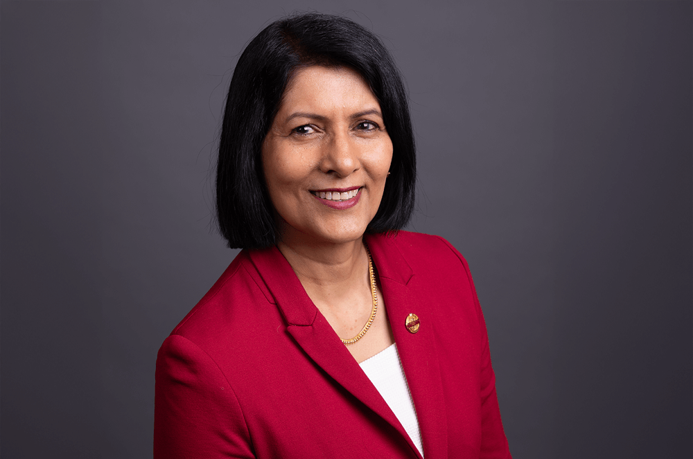 Toastmasters International President Radhi Spear in red suit jacket with Toastmasters pin