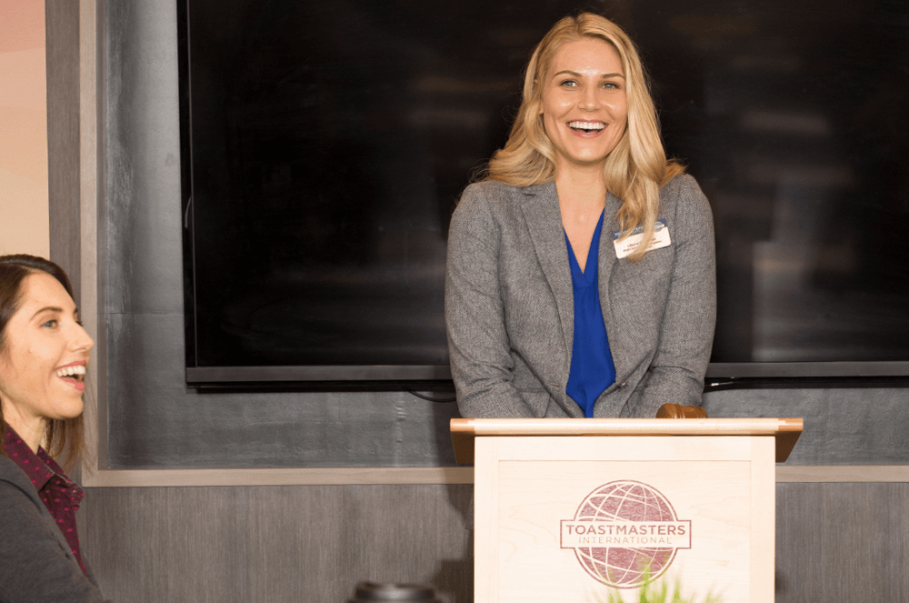 Woman standing at lectern with the Toastmasters logo