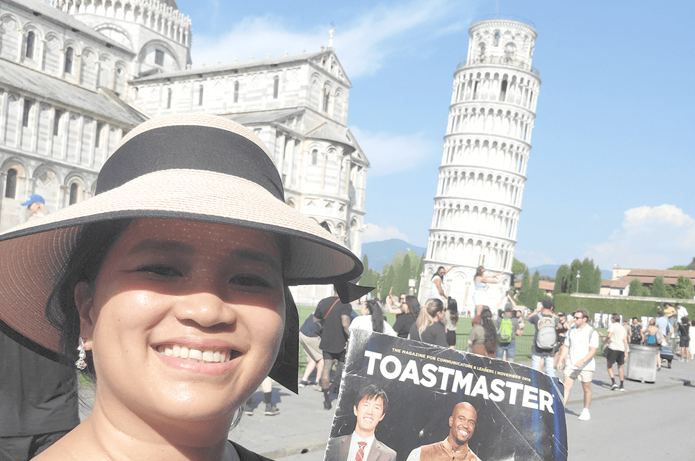 Woman smiling and holding a magazine in front of the Leaning Tower of Pisa