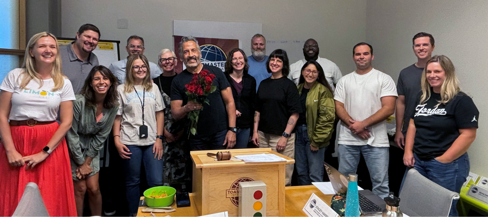 Man standing with flowers surround by Toastmasters club members