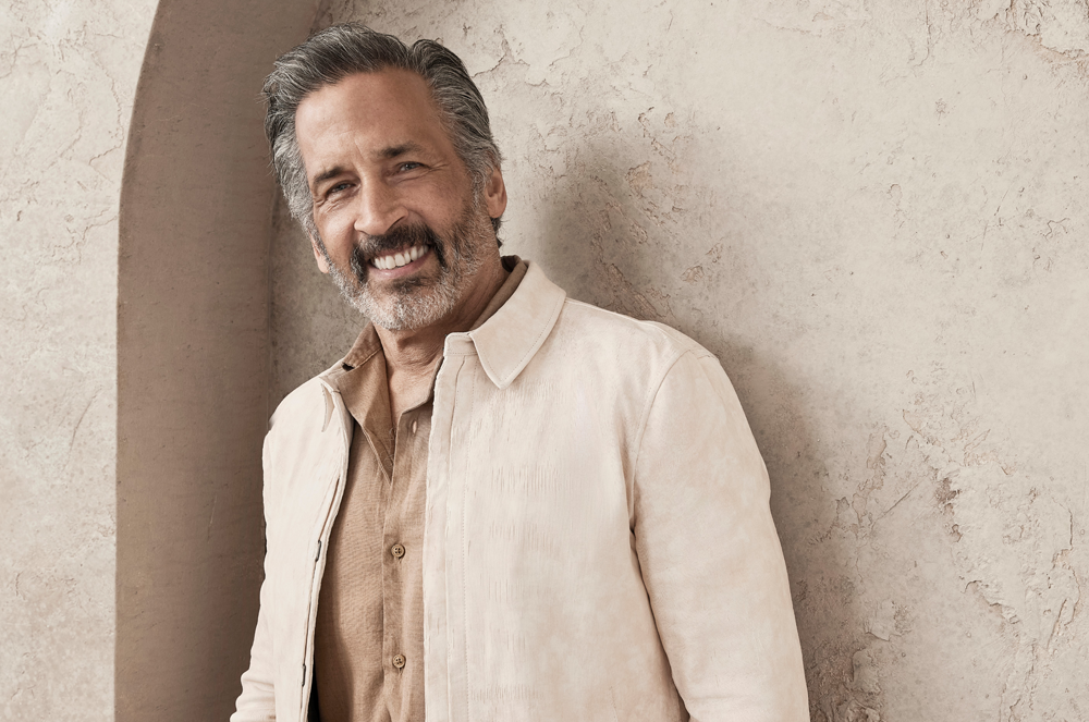 Man standing in linen jacket leaning against a wall