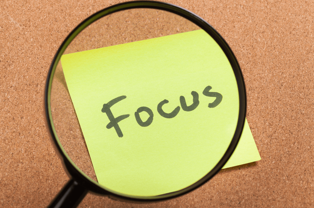 A magnifying glass looking at the word “focus” on a sticky note