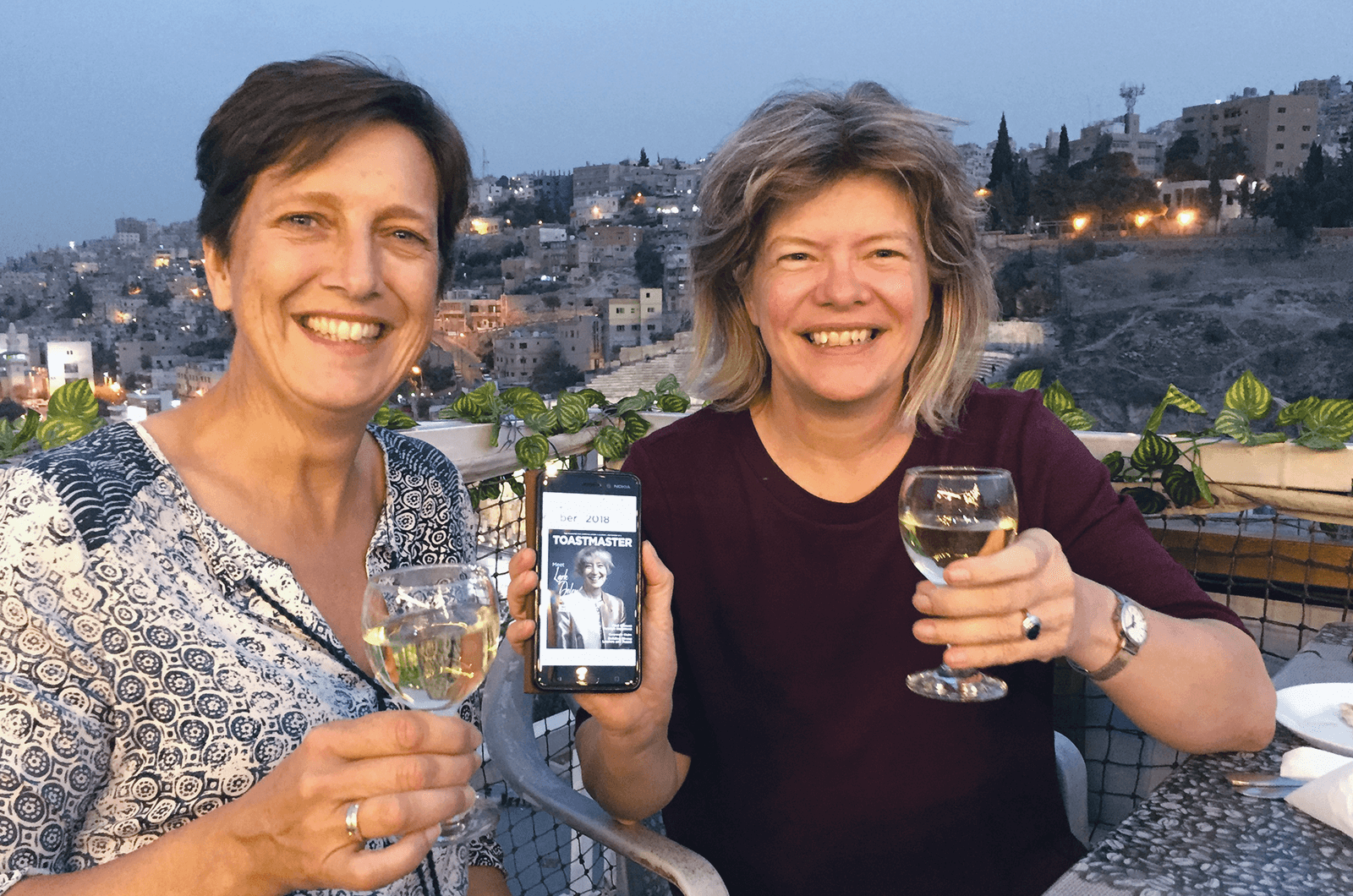 Lilian Van der Gugten, Dtm, left, and Lucy Sennef, ACS, ALB, of Apeldoorn, Netherlands, show the online Toastmaster magazine on a rooftop overlooking Amman, Jordan.