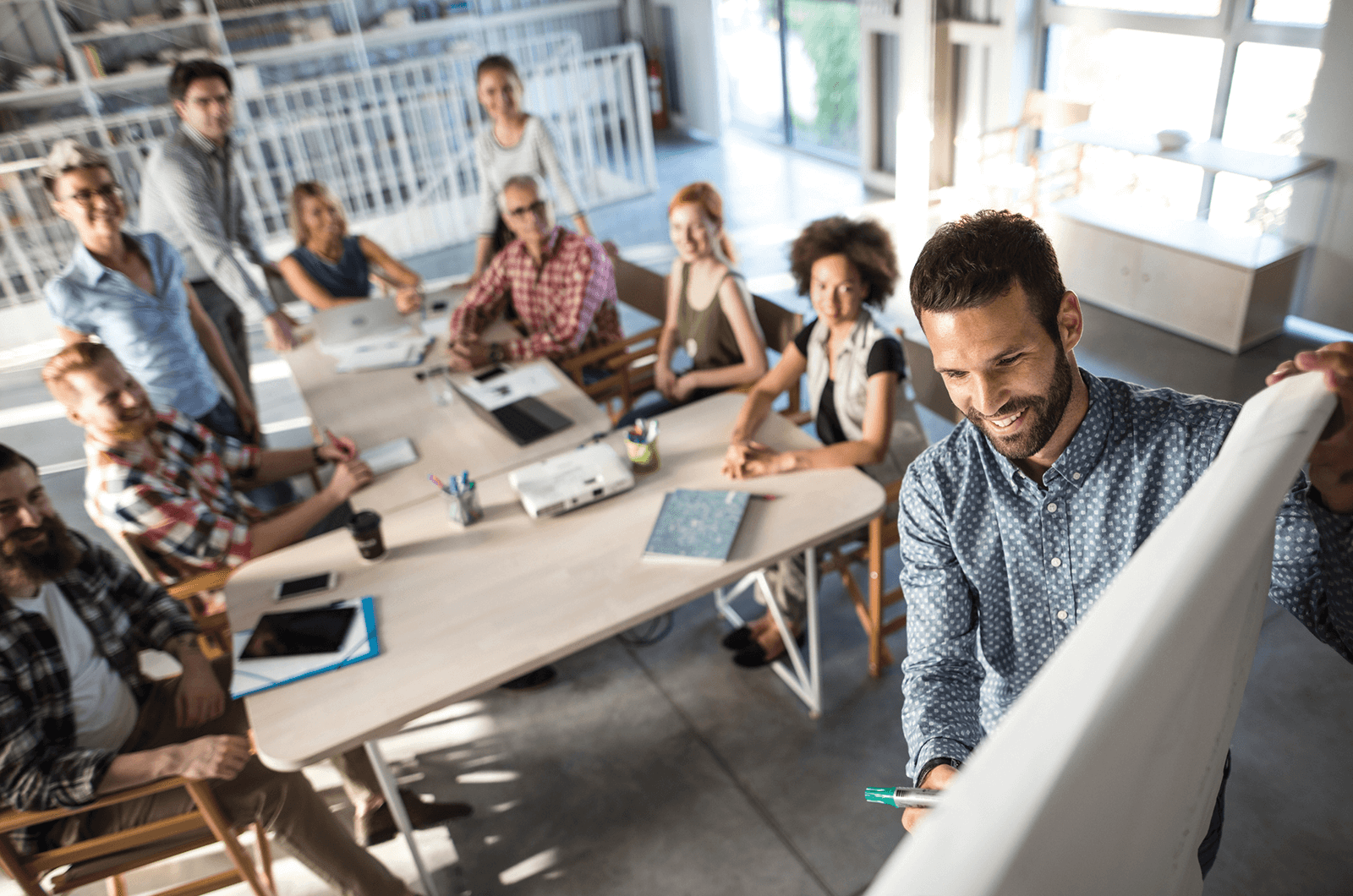 Group of people sitting at desk watching man lead meeting