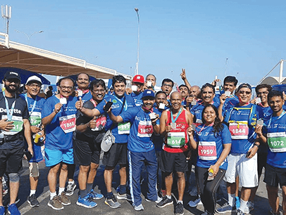 Members of Khimji Toastmasters in blue shirts pose after running Muscat Marathon