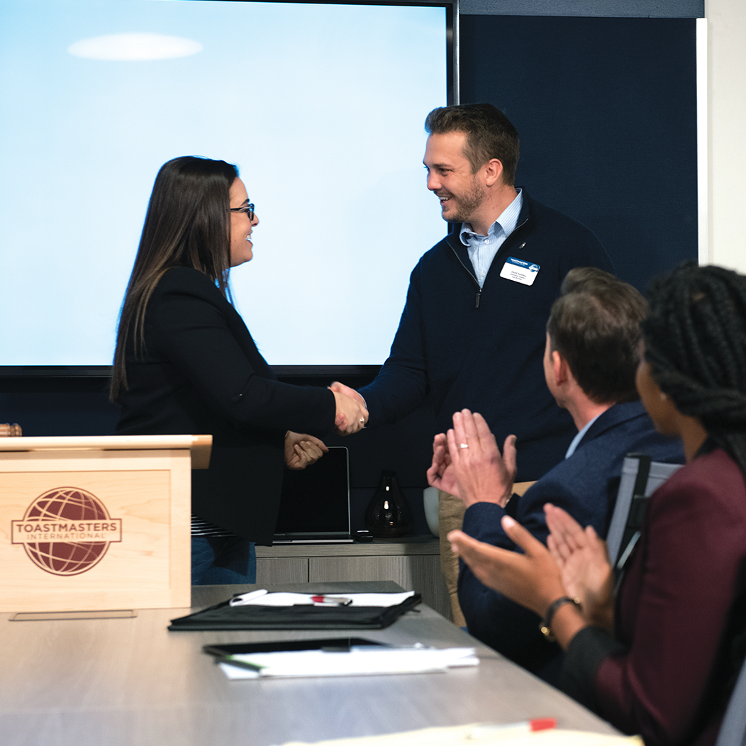 Woman at lectern shakes hands with man 