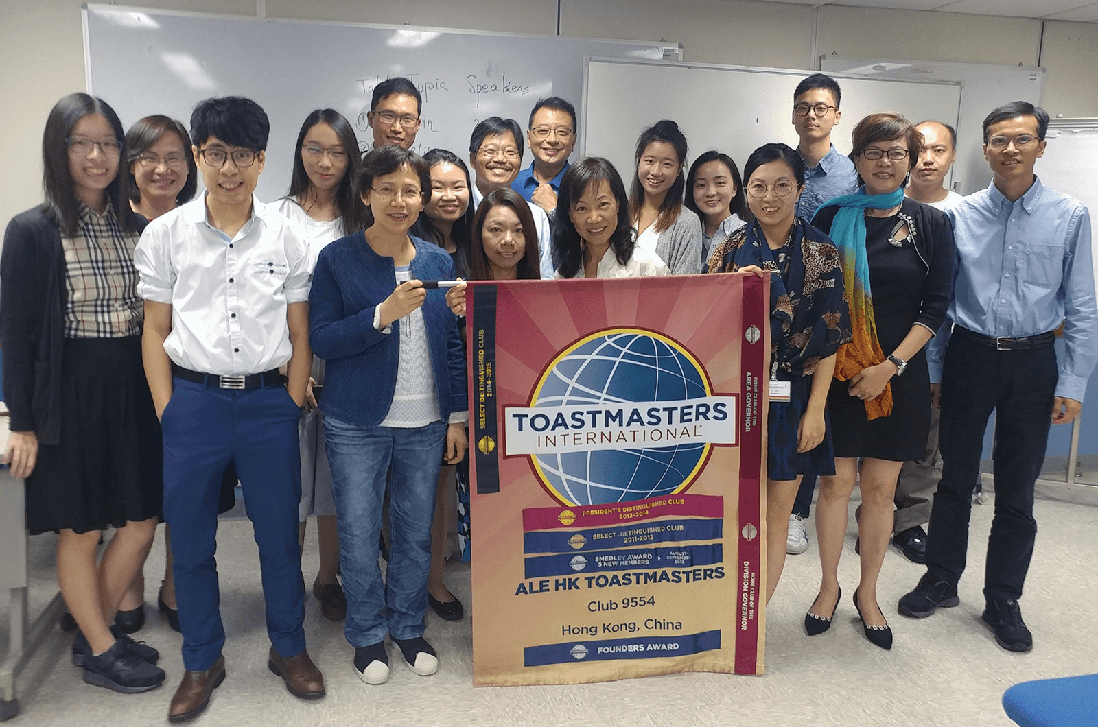 Group of Toastmasters members standing with club banner