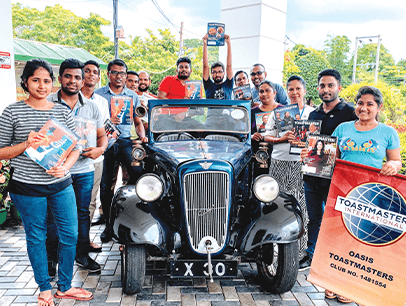 Toastmasters members holding magazine while posing next to 1927 car