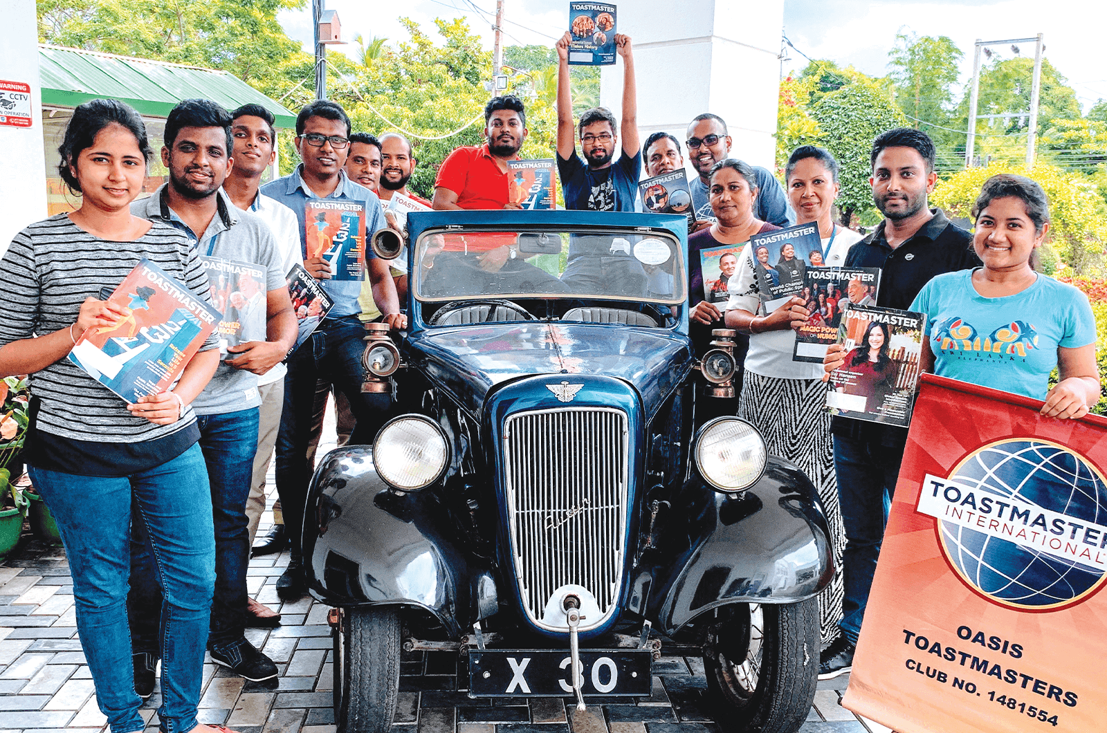 Toastmasters members holding magazine while posing next to 1927 car