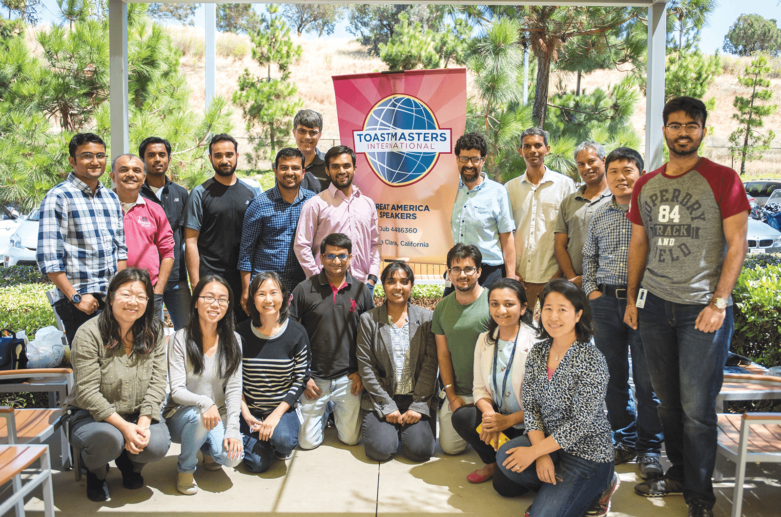 Group of Toastmasters members posing outdoors with banner