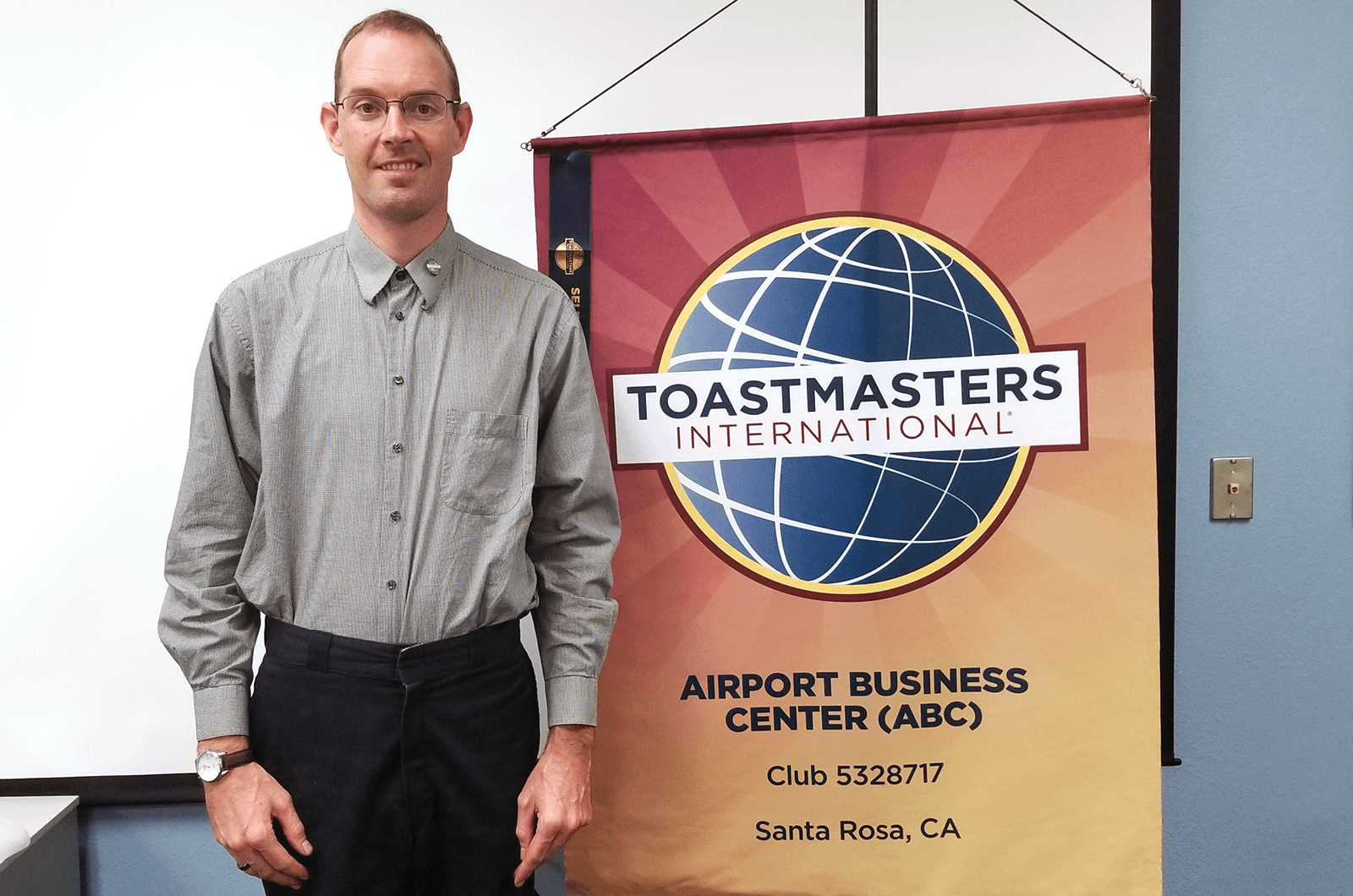 Toastmaster member standing next to club banner