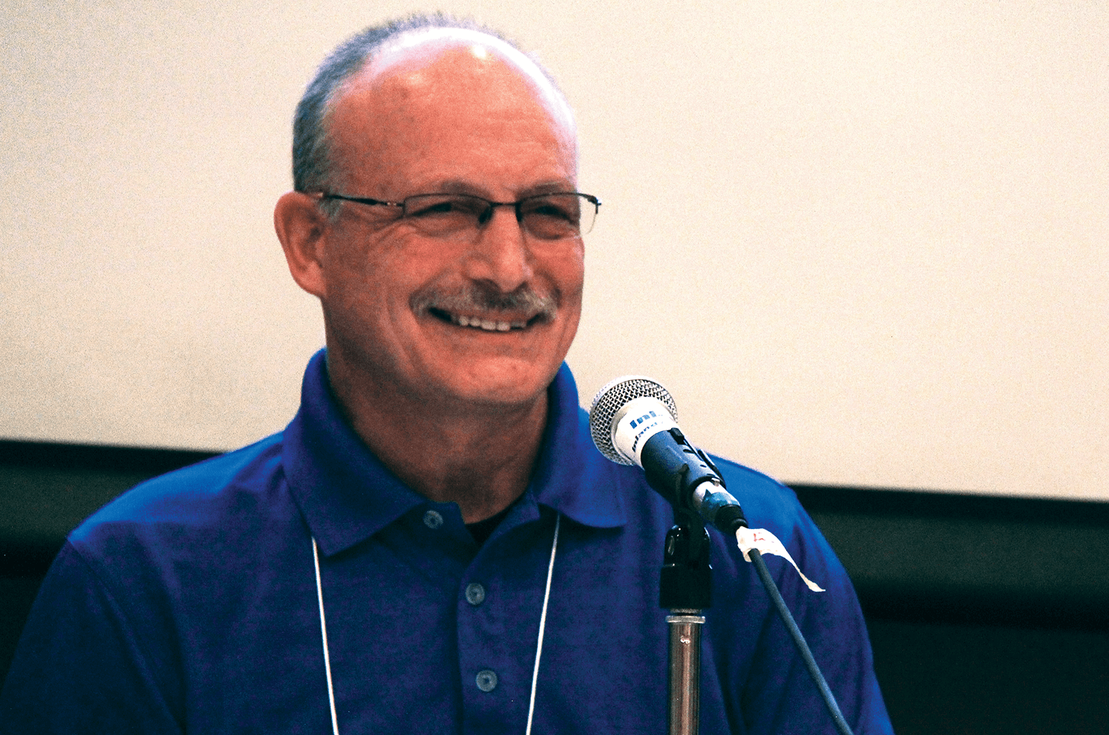 Man in blue shirt smiling in front of microphone