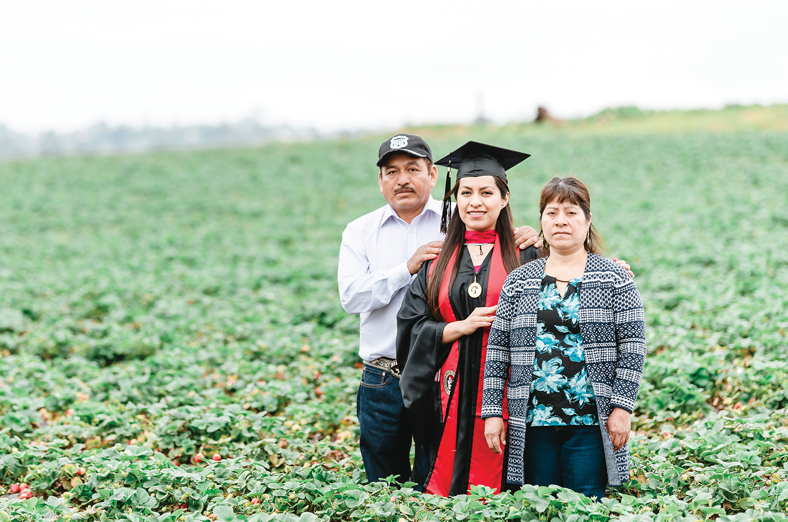 College grad stands in fruit field with parents