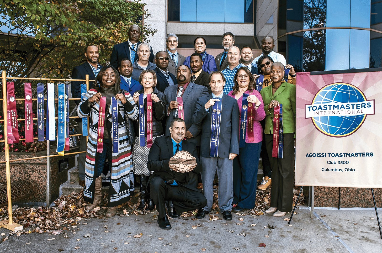 Group of Toastmasters members standing outside next to banner and ribbons