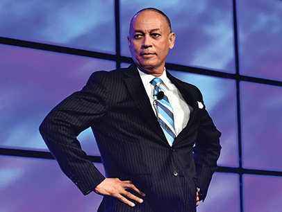 Ed Tate dressed in a suit and tie strikes a power pose onstage