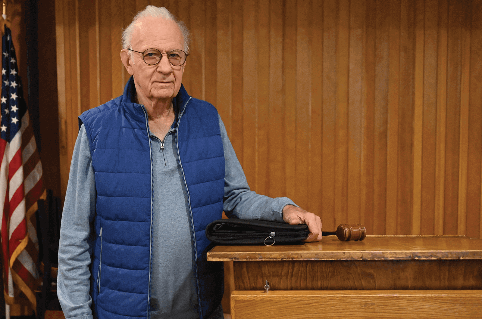 Man in blue vest standing at lectern with gavel