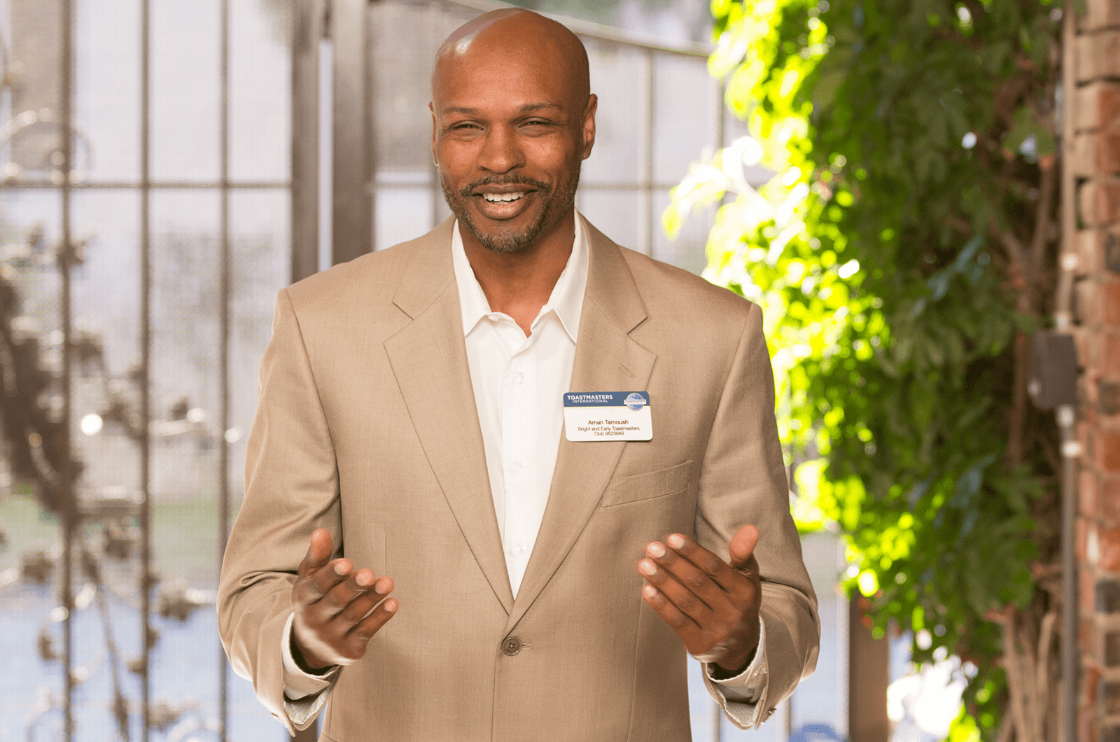 Man in tan suit jacket speaking with gestures