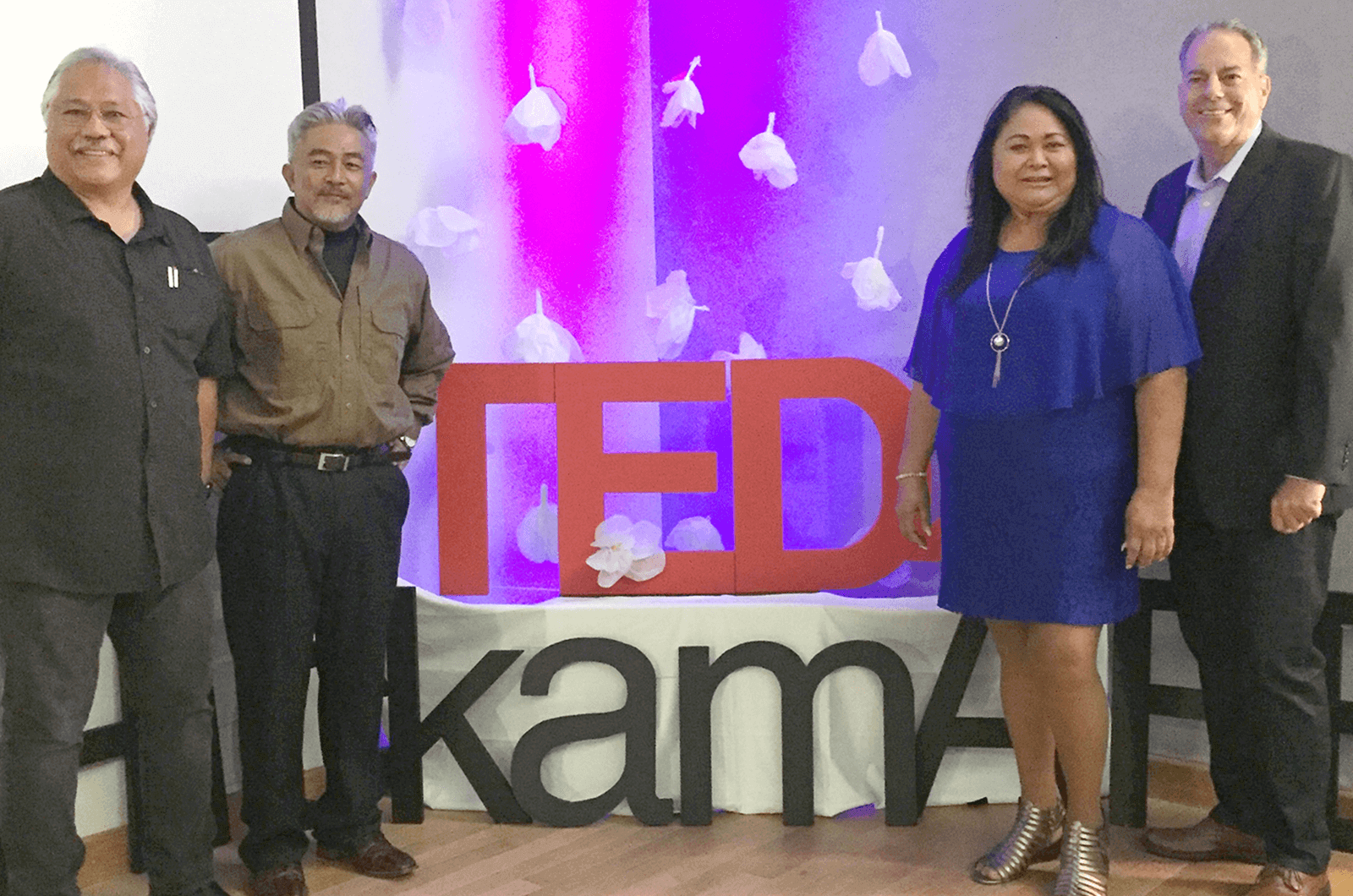 Three males and a female posing near TEDx sign