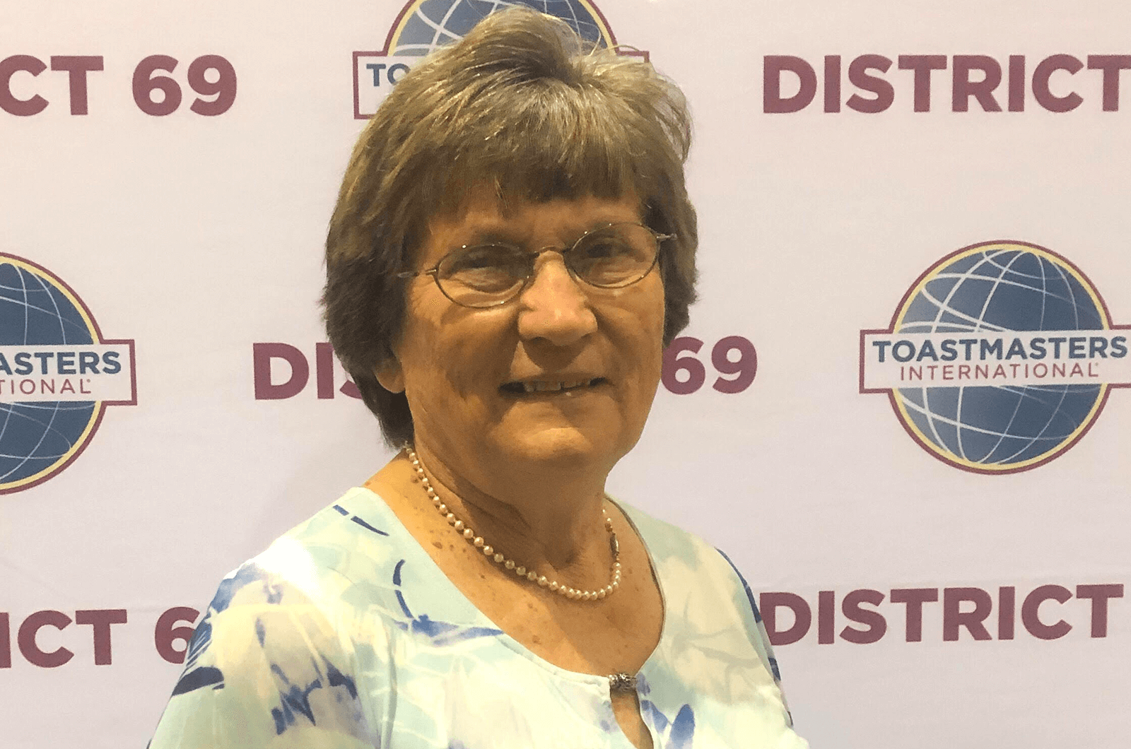 Barbara Nielsen poses in front Toastmasters banner