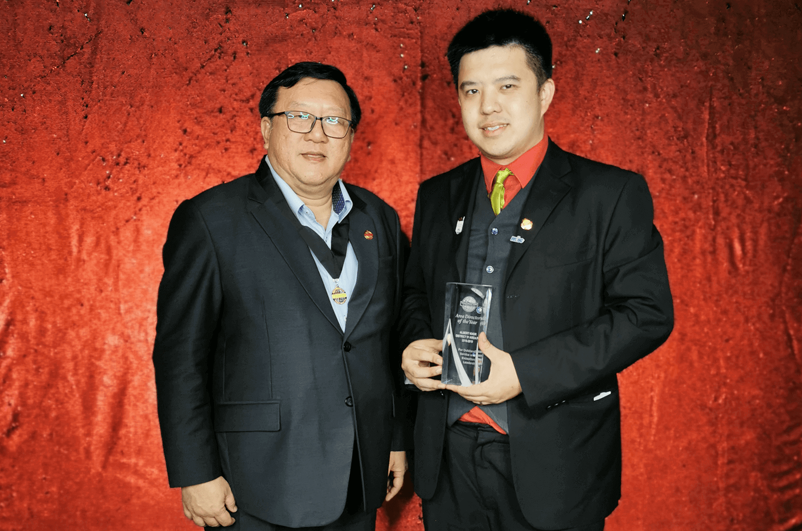 Men in black suits with red backdrop holding trophy onstage