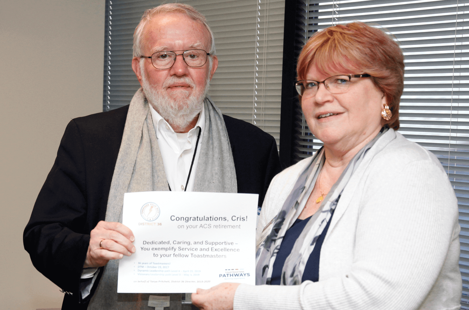 Man in scarf holding onto a certificate with a woman in white sweater