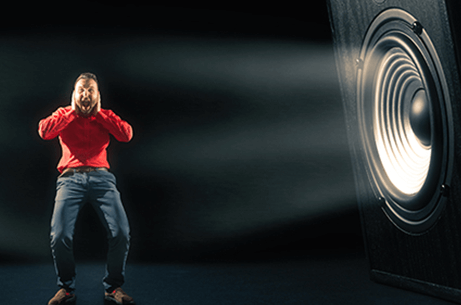 Man in red shirt holding hands over ears with speaker on side of him