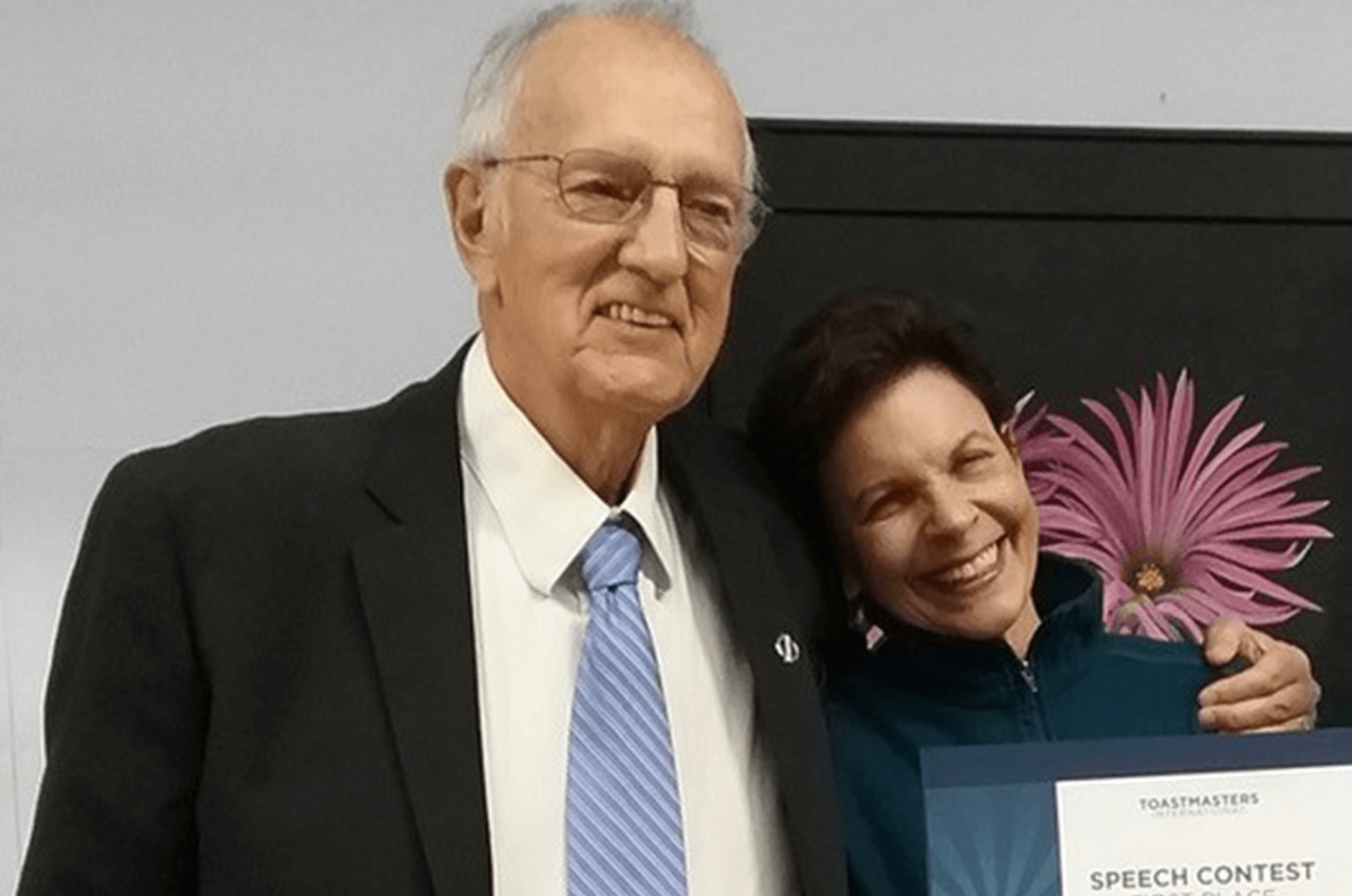 Man in blue tie with arm around woman holding certificate