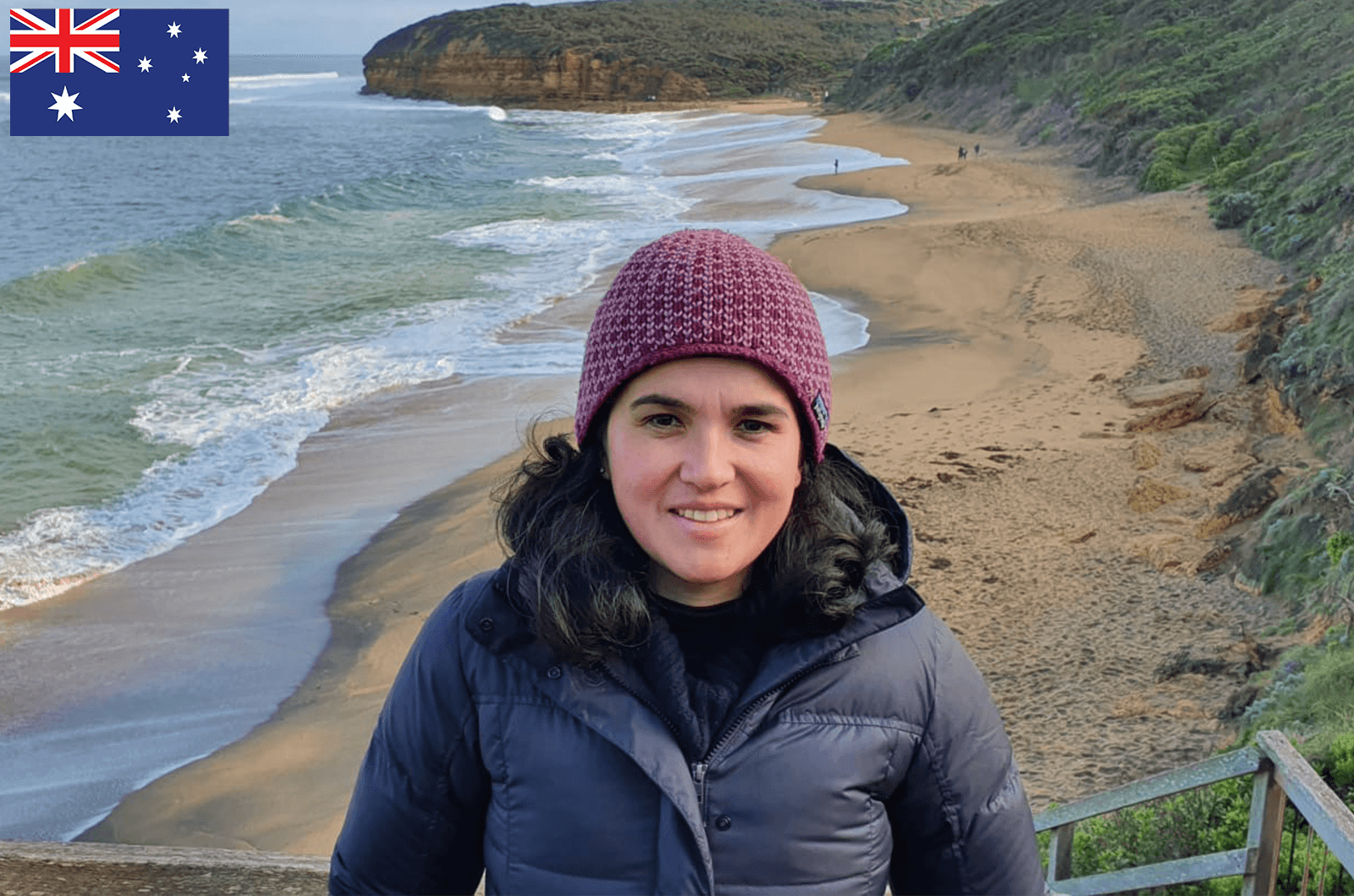 Woman in coat and hat with ocean and beach behind her