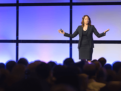 Woman speaking onstage with hands up