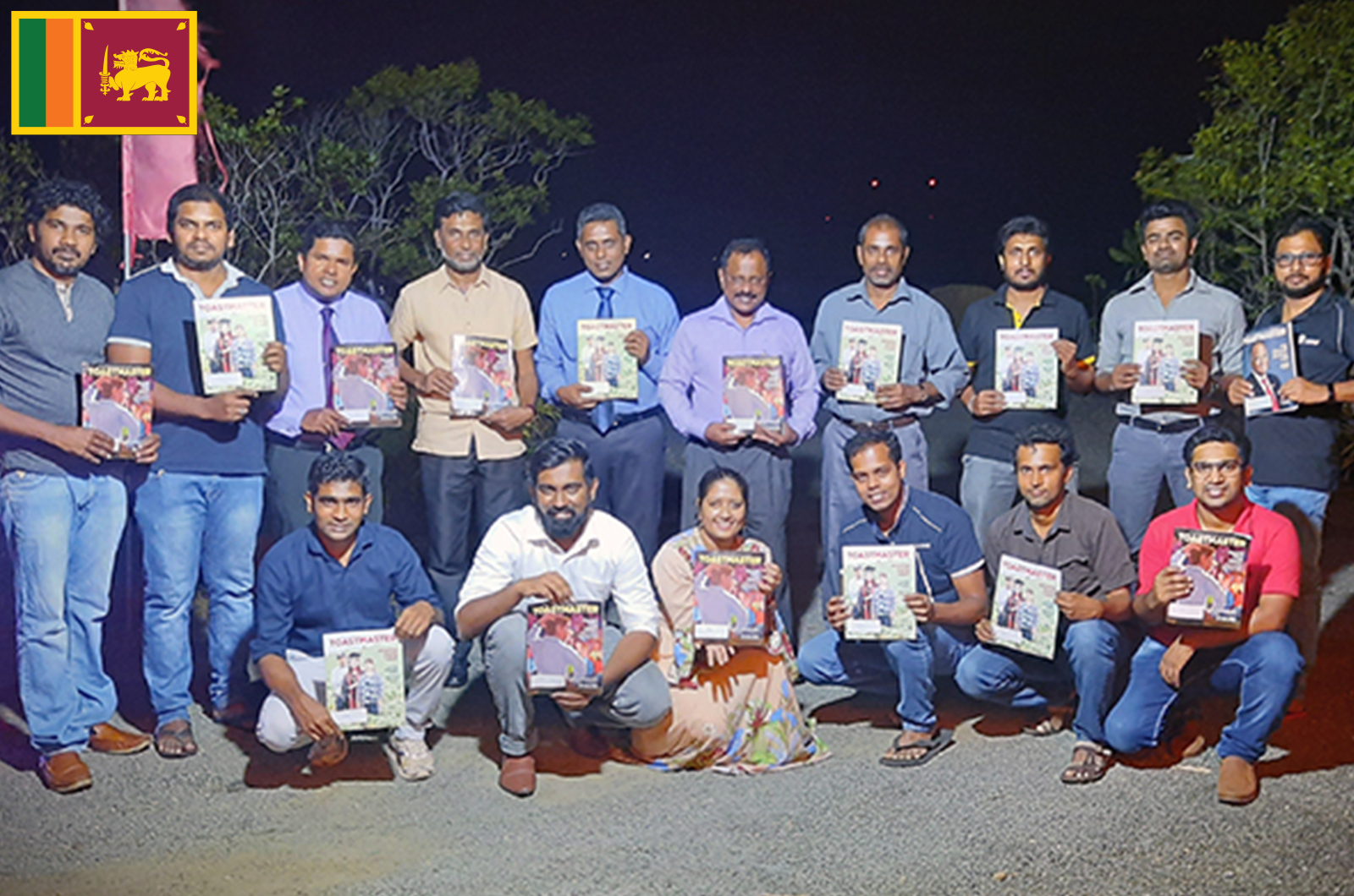 People standing outdoors at night holding Toastmaster magazines