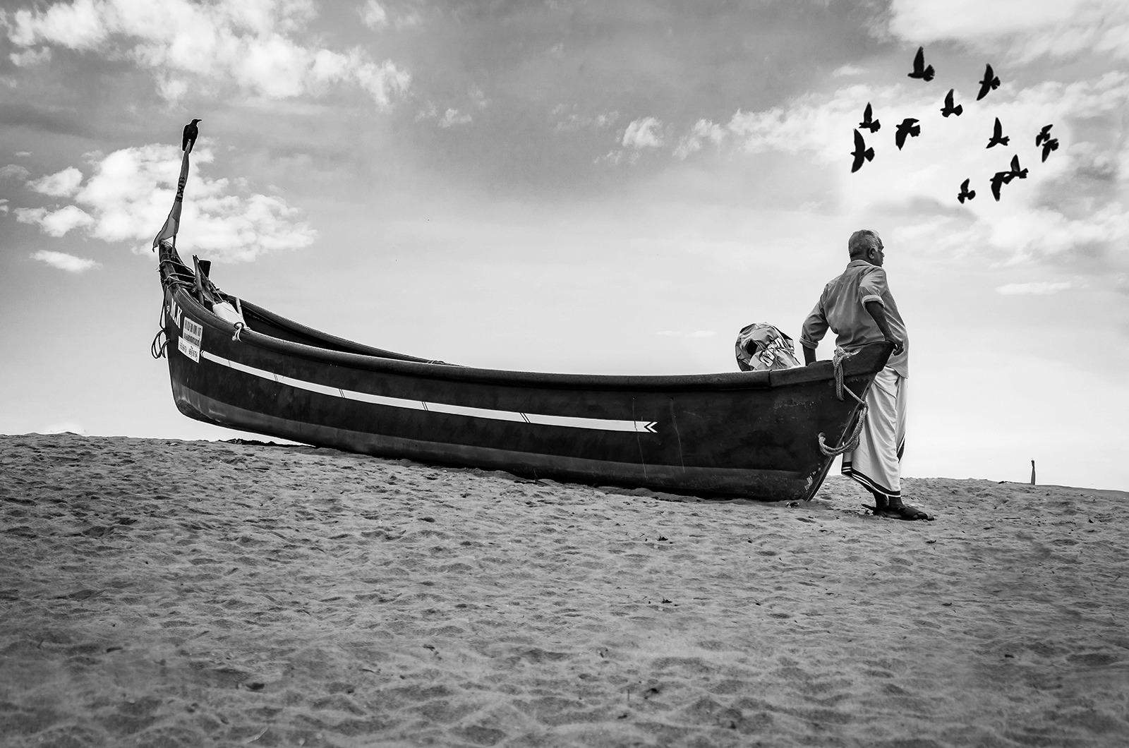 Black and white image of man on beach staring at the sea