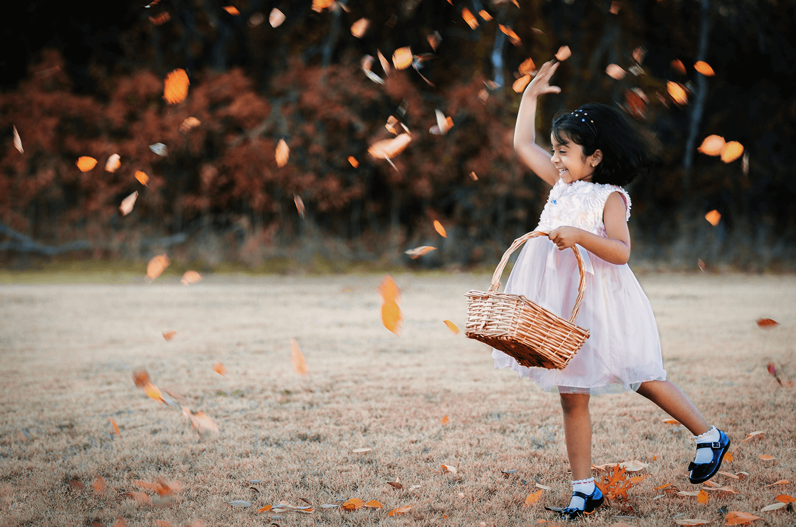 Little girl holding basket and throwing leaves in the air