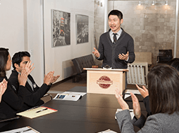 Man standing at lectern speaking to group of people clapping